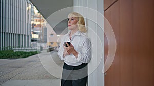 Aged businesswoman waiting meeting holding smartphone on street. Elderly woman