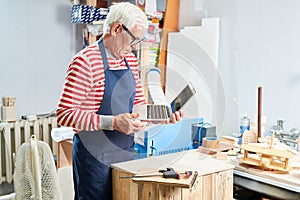 Aged carpenter with laptop in workshop