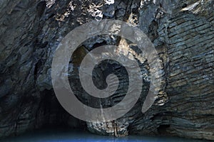 An aged cave interior. A rock wall and a lake