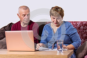 Aged couple going about their business, woman reading a newspaper and man opened laptop and sitting near his wife. photo