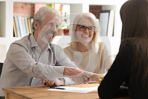 Aged couple handshaking with female relator closing successful deal