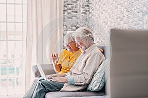 Aged couple sitting on couch in living room country house make videocall look at pc screen wave hands greeting friend, grown up