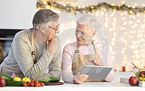 Aged Couple With Tablet Ordering Food Online In Kitchen