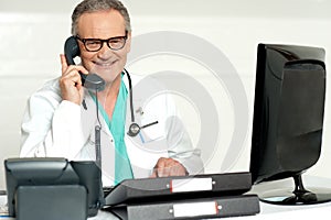 Aged doctor attending call in front of lcd screen