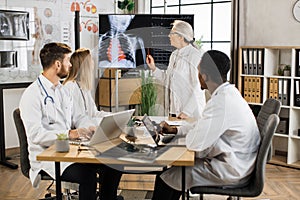 Aged doctor discussing with multiracial colleagues xray scan