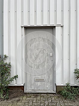 Aged door in an industrial setting with weed growing nearby