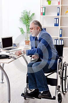 The aged employee in wheelchair working in the office