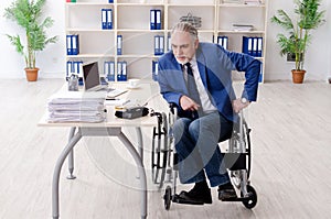 The aged employee in wheelchair working in the office