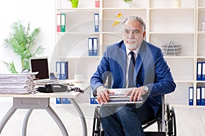 Aged employee in wheelchair working in the office