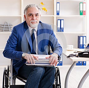 Aged employee in wheelchair working in the office