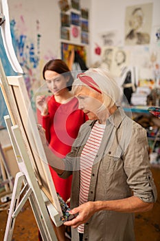 Aged famous artist painting near her dark-haired student