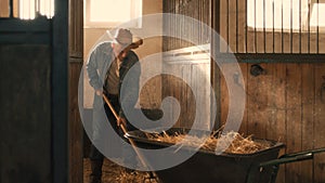 Aged farmer cleaning stall from hay