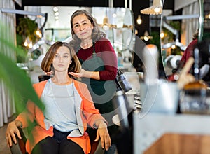 Aged female hairdresser offering modern hairstyling to young woman