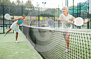 Aged female paddle tennis player performing backhand on outdoor court