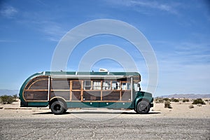 Aged green school bus on a dirt road in the desert against a blue sky