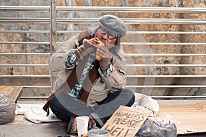 Aged homeless begger eating bread on the bridge