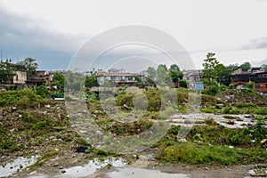 Aged houses behind weedy ground in cloudy spring after rain