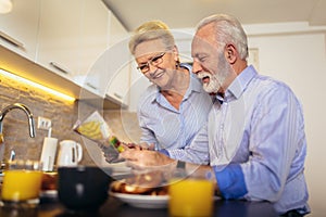 Aged loving couple reading newspaper at home