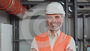Aged male factory worker in uniform crossing arms and smiling at camera