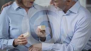 Aged male giving small present box to female, woman opening it and kissing man