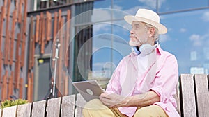 Aged male resting on wooden bench with tablet in hands