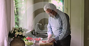 Aged man cutting fresh tomatoes cooking vegetable salad in kitchen