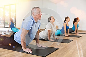 Aged man doing upward facing dog pose in yoga studio