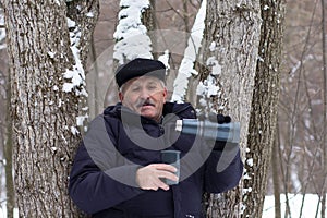 Aged man going to pour water from thermos into cup in the winter forest