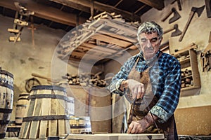 Aged man with grey hair does carpentry job in an old workshop