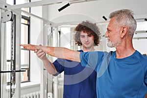 Aged man patient doing physiotherapy exercise under his male chiropractors control