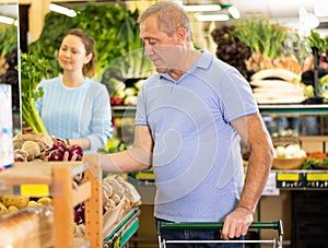 Aged man purchaser buying red onions in grocery store