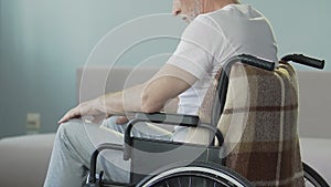 Aged man sitting in wheelchair looking at legs and nodding, lost ability to walk