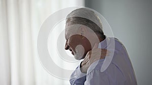 Aged man standing sideways, touching neck in acute pain, trying to move head