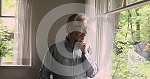 Aged man touch chink thinking while looking out the window