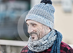 Aged man in winter hat and scarf. Portrait of smiling guy on street. Guy in knitted hat with ball