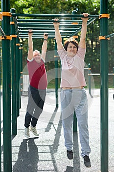 Aged man and woman doing exercises on sports bars in open-air sports area
