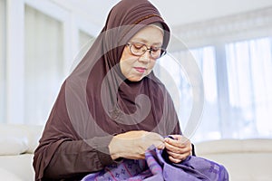 Aged Muslim woman sewing a cloth manually