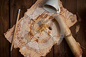 Aged parchment scroll, an old map, a pencil, and a spilled coffee cup on a wooden table.