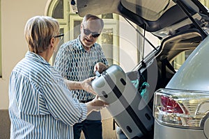 Aged people loading trolley in car trunk