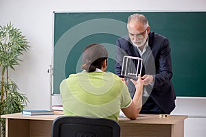 Aged physics teacher and male student in the classroom