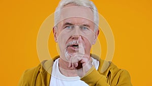 Aged retired man showing quiet gesture, holding finger lips, gossips secrecy