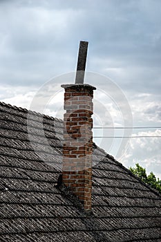 Aged roofing tiles with chimney on old house in village. A lot of moss on tiled roof of hovel against blue cloudy sky. Countryside