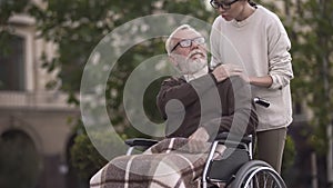 Aged sad disabled male in wheelchair covering young lady hand, family support