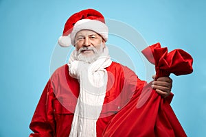 Aged Santa Claus carrying red bag full of christmas presents