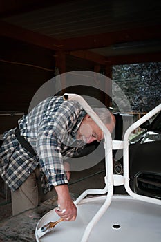 Aged senior man painting  carefully the back of  a garden  table