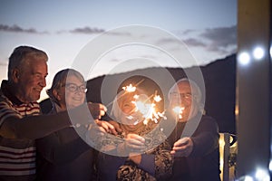 Aged senior people friends have fun and celebrate by night with fire sparkler - concept of new year eve and mature retired couples