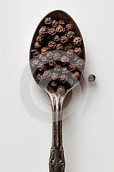 Aged Silver Spoon Filled with Whole Black Peppercorns on White Background