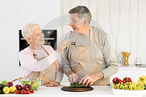 Aged Spouses Cooking Tasting Food Feeding Each Other In Kitchen