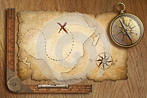 Aged treasure map, ruler and old gold compass on wooden table