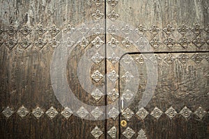 Aged two-leaf wooden door with metal ornaments simulating flowers and forming patterns